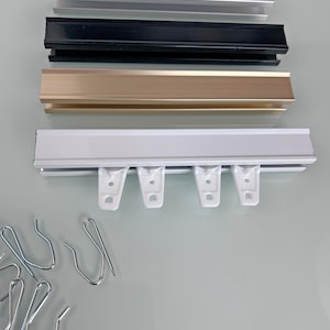 Puede incluir: Una variedad de rieles para cortinas en plata, negro, dorado y blanco. El riel blanco tiene ganchos de plástico blanco. También se ven varios ganchos de cortina de metal plateado.