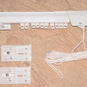 May include: A white curtain track system with mounting brackets and a pull cord. The track has multiple slots for curtain hooks. Two white mounting brackets are included. The cord is white and coiled.