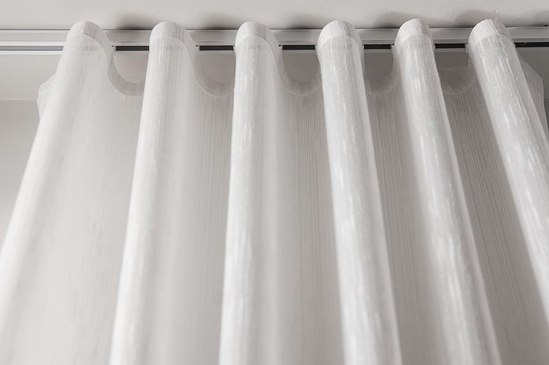 Close-up of perfect s-fold waves - sheer white curtain hanging from a slim white ripple fold ceiling track, showing the uniform wave fold heading and soft drape