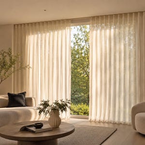 Cream sheer s-fold drapery panels gliding across a wide window wall on a discreet ceiling track - even wave folds in a neutral contemporary living room