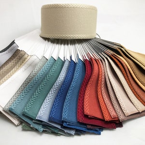 May include: A fan-shaped color chart of woven trim samples. The trim is a herringbone pattern with a contrasting edge. The colors range from white to beige, light blue, dark blue, red, orange, and brown.