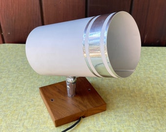 May include: A vintage white and silver accent lamp with a cylindrical shade. The lamp features a wooden base and a chrome stem. The lamp is connected to a black cord with an on/off switch. The lamp is approximately 10 inches tall.