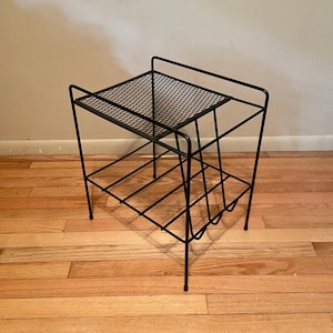 May include: Black metal side table with a wire mesh top and three shelves. The table has a geometric design and is made of thin metal.