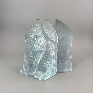 Puede incluir: Un par de sujetalibros de vidrio esmerilado con forma de elefantes. Los sujetalibros son de color azul claro y tienen una superficie texturizada.