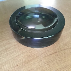 Può includere: Un posacenere circolare nero con una finitura liscia e lucida. Il posacenere ha un pozzetto rotondo e profondo per contenere i mozziconi di sigaretta.