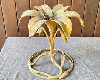 May include: A gold metal decorative stand in the shape of a lily flower. The stand has a round base and a delicate, intricate design.