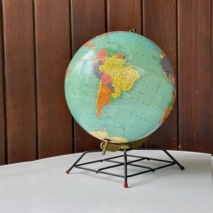 May include: A vintage green globe with a black metal stand. The globe shows the continents and oceans of the world.