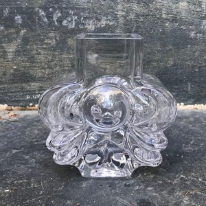 May include: A clear glass vase with a unique, intricate design. The vase has a square opening and a rounded, textured base.