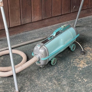 Puede incluir: Una aspiradora vintage azul y blanca con una manguera larga y una barricada de carretera a rayas rojas y blancas con el texto "DIETZ 337" en ella.