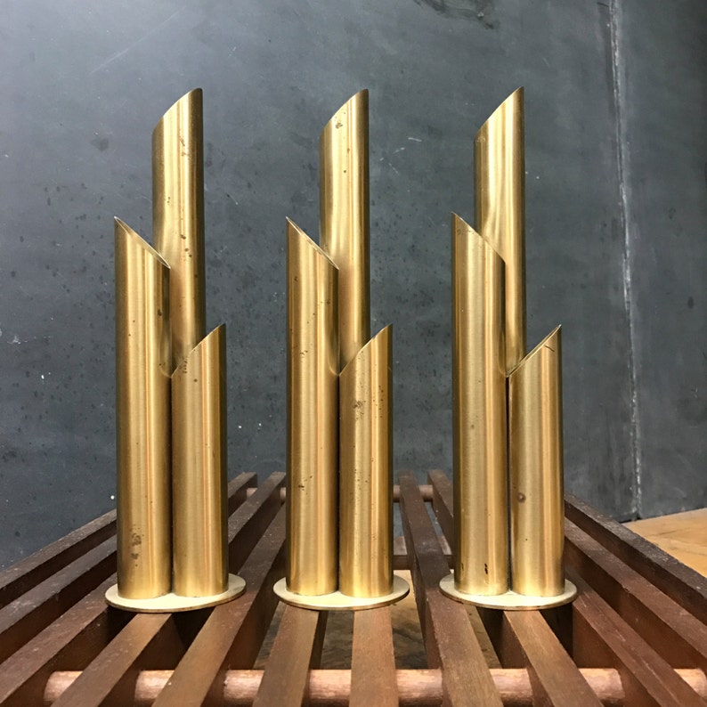 May include: Three gold metal vases with a geometric design. Each vase is made of four stacked cylinders, creating a modern and minimalist look.