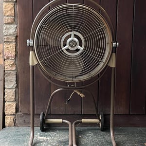 Peut inclure: Un grand ventilateur oscillant en m&eacute;tal brun avec une cage ronde en fil de fer et un cordon noir. Le ventilateur est sur roulettes et poss&egrave;de un pied &agrave; deux pieds.