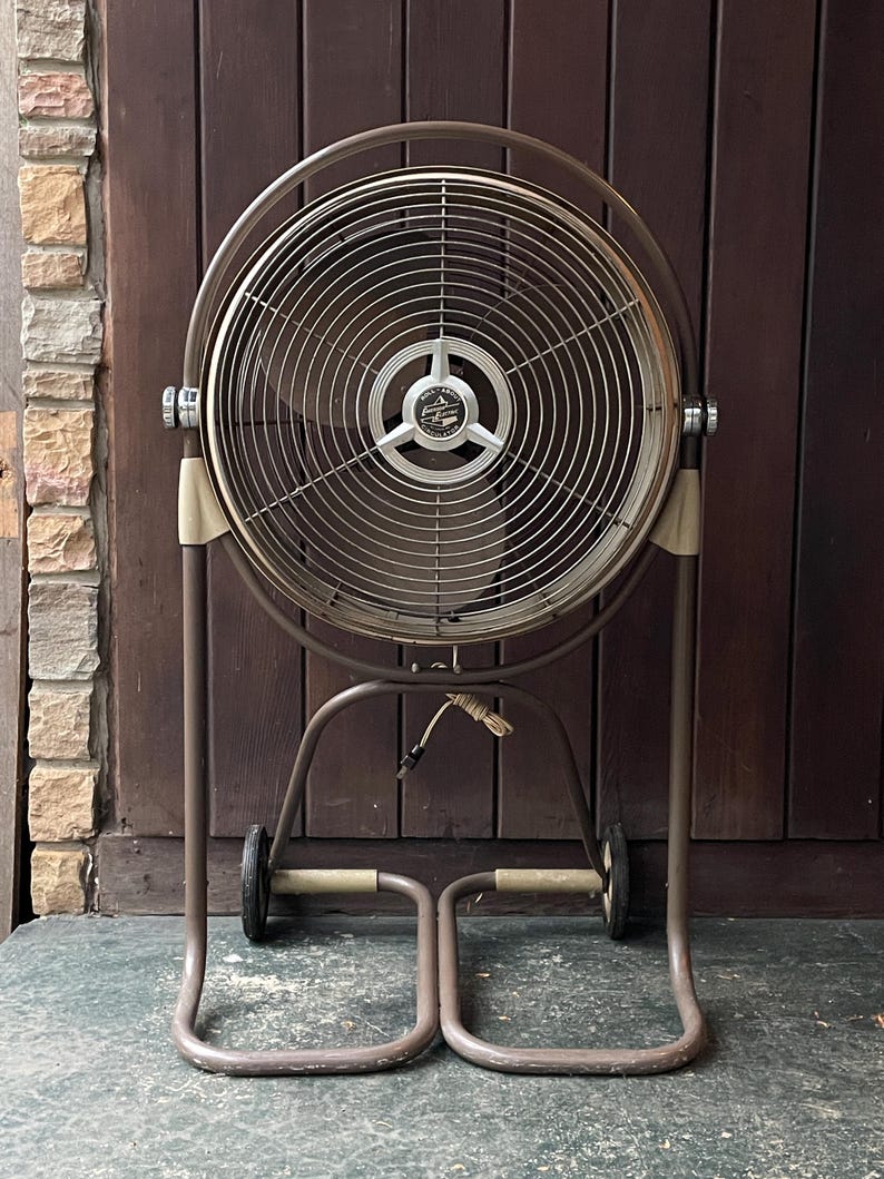 Peut inclure: Un grand ventilateur oscillant en m&eacute;tal brun avec une cage ronde en fil de fer et un cordon noir. Le ventilateur est sur roulettes et poss&egrave;de un pied &agrave; deux pieds.