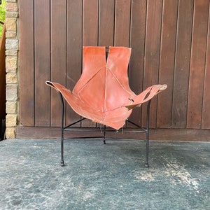 May include: A red leather chair with a black metal frame. The chair is in a leaf shape and has a unique design.