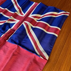 May include: A red, white, and blue flag with a Union Jack design. The flag is made of a soft, silky material and has a slightly faded appearance.