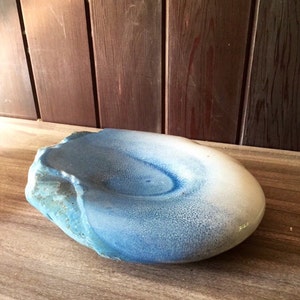 May include: A blue and white ceramic bowl with a textured surface. The bowl is shaped like a rounded oval and has a slight indentation in the centre.