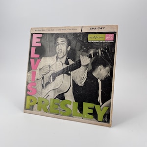 May include: Vintage Elvis Presley album cover. The album cover features a black and white image of Elvis singing and playing a guitar. The album title is in pink and green lettering.
