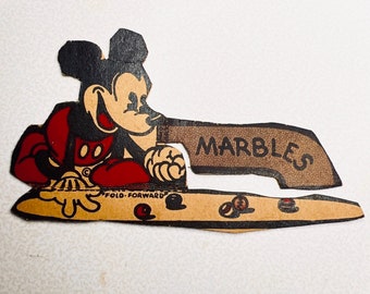 May include: Vintage Mickey Mouse die-cut cardboard advertisement. Mickey is in his classic red shorts and black ears. The brown sign reads "MARBLES". The bottom of the cardboard reads "FOLD FORWARD".