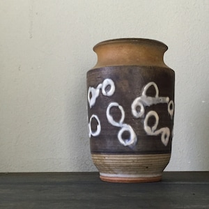 May include: A brown ceramic vase with a white glaze design. The vase has a rounded body and a flared lip.