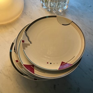 May include: A set of three ceramic plates with a geometric design in shades of blue, red, and beige. The plates are stacked on top of each other.