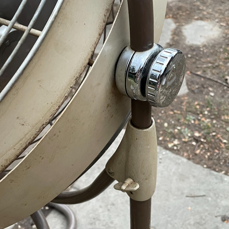 Peut inclure: Un ventilateur oscillant vintage en m&eacute;tal blanc avec une base en m&eacute;tal brun et un bouton de r&eacute;glage chrom&eacute;. Le ventilateur a une cage circulaire en fil m&eacute;tallique et une grande pale ronde.