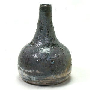 May include: A dark gray ceramic vase with a bulbous body and a narrow neck. The vase has a textured surface with small holes and a speckled glaze.