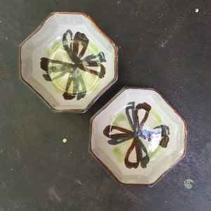 May include: Two octagonal ceramic bowls with a white glaze and brown and green floral designs.