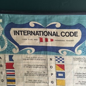以下が含まれることがあります： 国際的な海上信号旗のヴィンテージチャート。チャートには、旗とその対応する意味が表示されています。旗は赤、白、青、黄色の4色です。チャートは青と白の布に印刷されています。