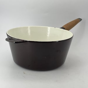Può includere: Una casseruola smaltata marrone scuro con interno color crema. La casseruola ha un manico in legno e un piccolo manico laterale. Questa pentola in stile vintage è ideale per cucinare.