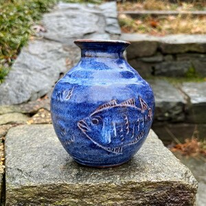 May include: A small blue ceramic vase with a fish design. The vase has a glazed finish and a rounded shape.