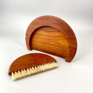 May include: A wooden dustpan and brush set in a half-moon shape. The dustpan is made of dark wood with a smooth finish. The brush has natural bristles and a wooden handle.