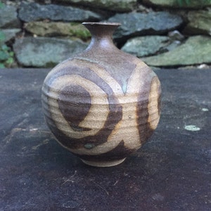 May include: A small, round, brown ceramic vase with a white and brown swirl design. The vase has a narrow neck and a wide base.