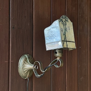 May include: A vintage wall-mounted light fixture with a frosted glass shade featuring a bamboo and bird design. The fixture is made of brass and has a decorative scroll arm.
