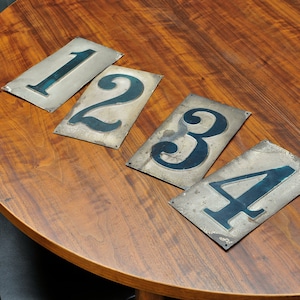 Puede incluir: Cuatro placas de metal con los números 1, 2, 3 y 4 pintados en azul sobre una mesa de madera.