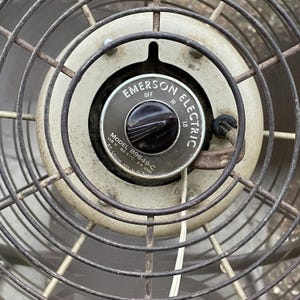 Peut inclure: Gros plan sur un ventilateur vintage Emerson Electric avec un bouton noir et une grille en m&eacute;tal blanc. Le ventilateur porte le num&eacute;ro de mod&egrave;le 89649-C et est con&ccedil;u pour 115 volts, 60 cycles et 2,9 amp&egrave;res. Le ventilateur est fabriqu&eacute; &agrave; St. Louis, Missouri, &Eacute;tats-Unis.