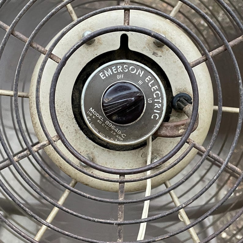 Peut inclure: Gros plan sur un ventilateur vintage Emerson Electric avec un bouton noir et une grille en m&eacute;tal blanc. Le ventilateur porte le num&eacute;ro de mod&egrave;le 89649-C et est con&ccedil;u pour 115 volts, 60 cycles et 2,9 amp&egrave;res. Le ventilateur est fabriqu&eacute; &agrave; St. Louis, Missouri, &Eacute;tats-Unis.