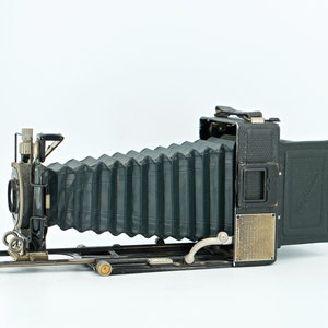 May include: A vintage black bellows camera with a leather bellows and a brass lens. The camera has a metal frame and a wooden back.