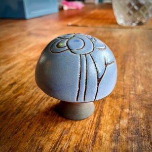 May include: A blue ceramic mushroom figurine with brown painted details. The mushroom has a rounded top with a stylized flower design and a short stem.