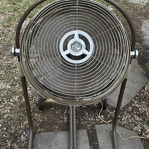 Peut inclure: Un ventilateur sur pied en m&eacute;tal brun avec une cage m&eacute;tallique circulaire et une pale de ventilateur ronde en m&eacute;tal argent&eacute;. Le ventilateur porte une &eacute;tiquette argent&eacute;e avec le texte "Full-About Electric Circulator".