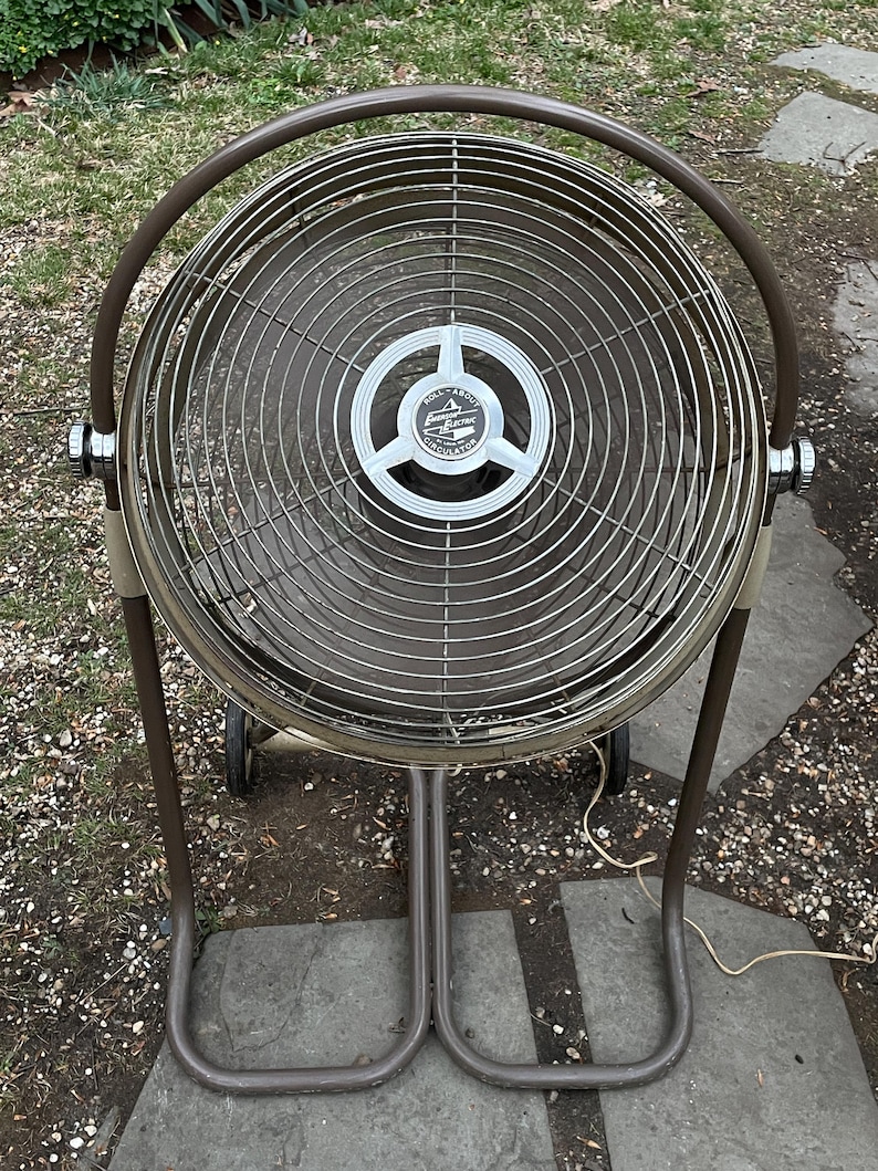 Peut inclure: Un ventilateur sur pied en m&eacute;tal brun avec une cage m&eacute;tallique circulaire et une pale de ventilateur ronde en m&eacute;tal argent&eacute;. Le ventilateur porte une &eacute;tiquette argent&eacute;e avec le texte "Full-About Electric Circulator".
