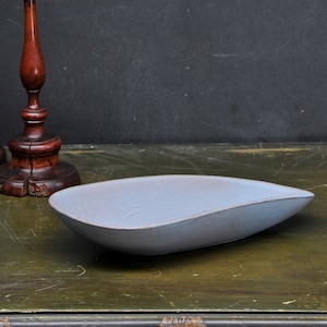 Könnte beinhalten: Eine hellblaue Keramik-Servierplatte mit leicht geschwungener Form. Die Platte liegt auf einer dunkelgrünen Holzoberfläche.