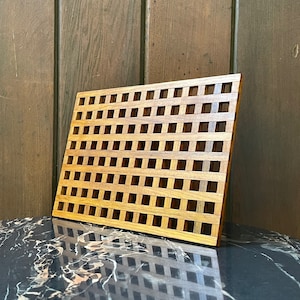 May include: A wooden decorative wall panel with a grid pattern. The panel is made of light brown wood and has a square shape.
