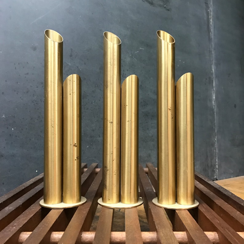 May include: Four gold metal vases, each with three cylindrical openings, arranged in a row on a wooden surface.