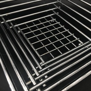 Könnte beinhalten: Nahaufnahme mehrerer glänzender, chromfarbener Metallgitter. Die Gitter sind rechteckig mit einem Gittermuster in der Mitte. Das Bild ist vor einem schwarzen Hintergrund aufgenommen.