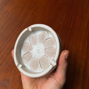 May include: White ceramic ashtray with a swirl design. The ashtray has a circular shape and a slightly raised rim.