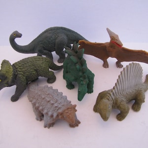 May include: A set of six plastic dinosaur toys, including a green triceratops, a green stegosaurus, a brown pterodactyl, a gray ankylosaurus, a green brachiosaurus, and a gray spinosaurus.