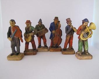 May include: Set of six hand-painted figurines depicting a band of musicians. Each figurine is wearing a different colored hat and playing a different instrument, including a violin, drum, accordion, bass, flute, and tuba.