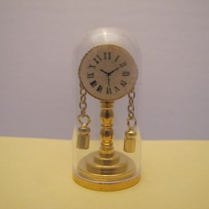 May include: A gold-toned clock with Roman numeral markings on the face, suspended from a chain and encased in a clear glass dome.