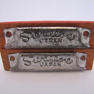 May include: Two vintage harmonicas with wooden cases and metal plates. The plates are silver and have the text "Sierallo" and "JAPAN" embossed on them.