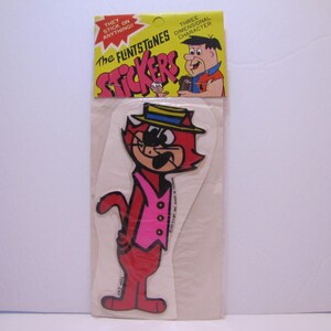 May include: A vintage pack of The Flintstones Stickers featuring a red cartoon cat wearing a pink waistcoat, a blue and yellow hat, and sunglasses. The pack says "They stick on anything!" and "Three Dimensional Character Stickers".