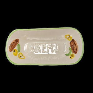 May include: A white ceramic bread dish with a green border and the word "BREAD" embossed in the center. The dish is decorated with painted images of bread, vegetables, and herbs.